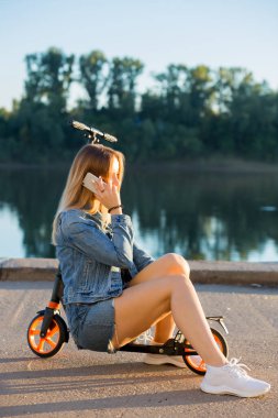 Doğada bir scooter üzerinde oturan ve Smartphone'da konuşurken öğrenci kız