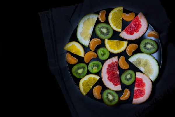 shredded bright vivid brilliant yellow green orange red grapefruit lemon orange Mandarin kiwi sweetie in a black plate on black background close up