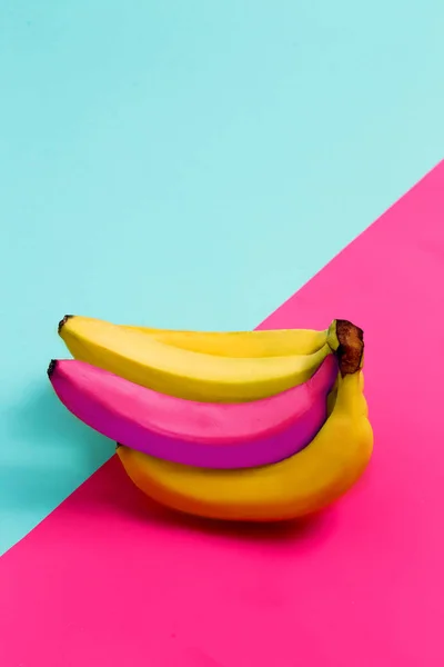 Banana group on pink, blue background. Colorful two tone background, a single pink banana among the yellow. The concept of uniqueness, one and only