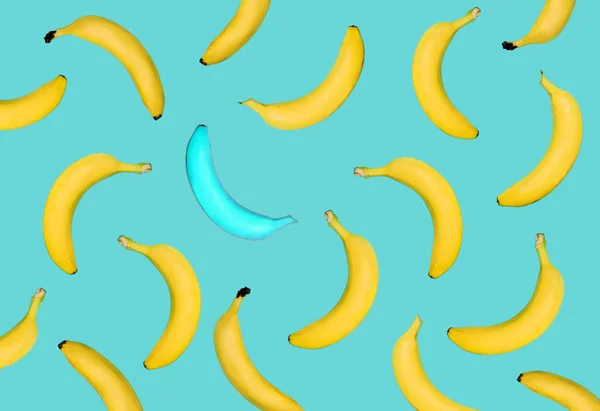 Outstanding blue banana among yellow banana on pastel blue background. Fruits fall from top to bottom