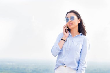 Evet ve doğa, gökyüzü arka plan gülümseyen bardakları ile mutlu moda kadın. Müzakerelerde Smartphone başarılı iş kadını