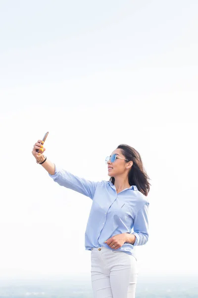 素敵な女性のスマート フォンとは Selfie を見て笑みを浮かべて白い空に対してカメラ路上 コピー スペース — ストック写真