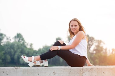 Beyaz gömlek ve siyah pantolon doğada günbatımında oturan güzel genç kadın portresi. Öğrenci yaşamı