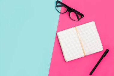 Düz yatıyordu, en iyi görünümü office tablo resepsiyon. Açık Not defteri, gözlük ve kalem kağıt pembe ve mavi zemin üzerine boşlukla kopya alanı ile çalışmak
