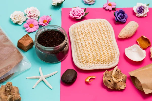 Closeup of colorful Spa and care facilities, small flowers, scrub, washcloth and seashells on pink and blue background