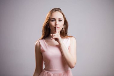 Pembe elbiseli güzel genç kız diyor ki sessizlik işareti ön plana tutan gösterilen Shhh, dudaklarında parmak. Gizli, sürpriz kavramı.