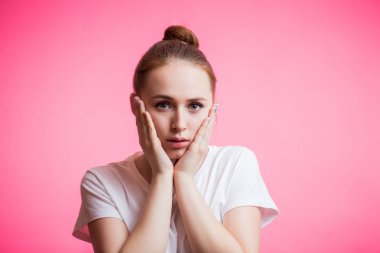 Kırmızı saçlarını topuz ve kameraya, pembe arka plan kopya alanı ile seyir sürpriz giyen bir güzel kız portresi. El palm yanak üzerinde tutan genç kadın