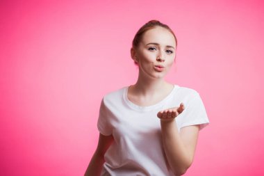 Güzel neşeli kırmızı saçlı kız pembe bir arka plan kopya alanı ile kameraya bir öpücük gönderir. İnsan duyguları, yüz ifadesi, sevinç, mutluluk kavramı