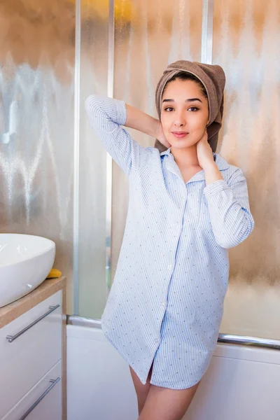 portrait of happy woman in shirt and a towel on head posing on the bathroom background