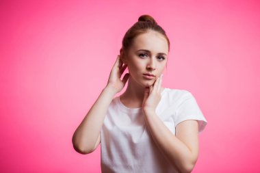 Beyaz t-shirt, pembe arka plan kameraya bakarak gülümseme ile rüya gibi şehvetli şirin kız. İnsan duyguları, yüz ifadesi kavramı