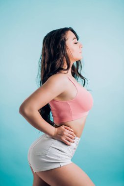 Sevimli gülümseyen esmer fitness kadın seksi giysileri yana kapalı gözler ile mavi bir arka plan üzerinde duruyor. Seks, dans, spor, fitness, twerk kavramı