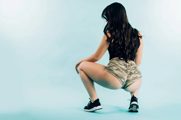 コピー スペースと青色の背景の上に座ってスタジオで戦利品ダンスを踊る魅力的なセクシーなブルネットの少女 — ストック写真