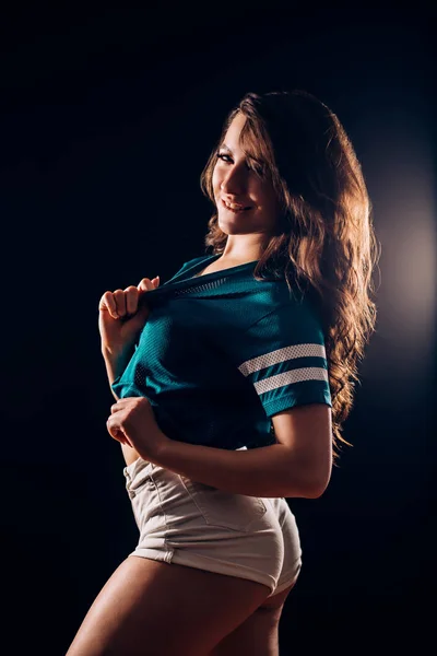 性感迷人的热黑发女人的肖像与长波浪形头发在短的白色短裤和蓝色 T恤在黑暗的黑色背景 苗条的身材 爱好概念 — 图库照片
