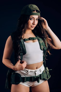 Moda güzel esmer kadın yeşil askeri giysiler ve Studio siyah bir zemin üzerine poz kısa beyaz şort