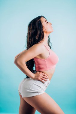 Sevimli gülümseyen esmer fitness kadın seksi giysileri yana kapalı gözler ile mavi bir arka plan üzerinde duruyor. Seks, dans, spor, fitness, twerk kavramı