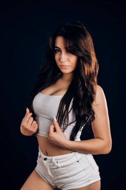 Güzel seksi fitness, siyah arka plan üzerinde dansçı kadın portresi. Sportif bir figür, uzun saçlı, beyaz şort ve kameraya bakarak bir bluz giyen genç bir kızla