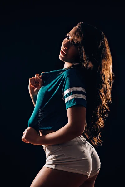 ショート パンツと黒の背景の青い シャツの美しいブルネットの女性の横向きの肖像画 セクシーな運動図 フィットネス ダンサーの女の子 — ストック写真