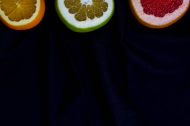 Narenciye üç tür portakal greyfurt canlarım yarı görünür altındaki Mutfak havlu koyu gri mavi siyah bir arka plan kopya alanı ile cut parçalar.