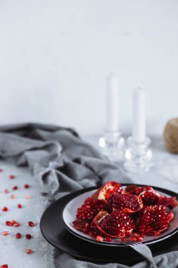 Tablo dekore edilmiş. Kırmızı olgun nar meyve mumlar ile gri bir tablo üzerinde siyah bir tabak içinde. Sağlıklı gıda, meyve ve sebze kavramı