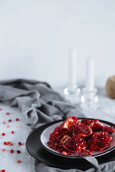 Beautifully decorated table. Red ripe pomegranate fruit in a black plate on a gray table with candles. Healthy food, fruits and vegetables concept