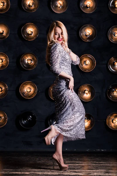 Siyah bir zemin üzerine uzun gümüş elbisenin içinde mutlu neşeli sarışın kadın. Lüks, parti, tatil, Güzellik, yeni yıl, Noel kavramı.