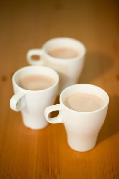 Three white cups of coffee, cocoa or latte on a wooden background on the table, closeup