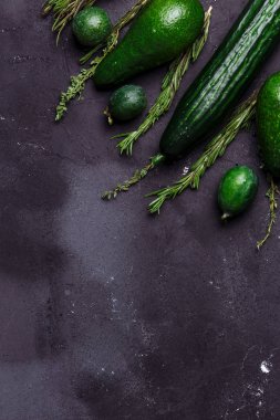 Yeşil sebze, meyve ve otlar ürün yelpazesine siyah arka plan üzerine. Alanı yukarıdan kopyalayın. Rosemary, kimyon, salatalık, avokado, feijoa mutfak masasında