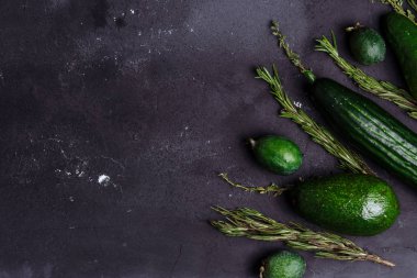 Siyah arka plan üzerinde yeşil sebze, meyve ve otlar çeşitleri. Kopya alanı Üst görünümü. Biberiye, kimyon, salatalık, avokado, mutfak masasında feijoa. Sağlıklı gıda kavramı