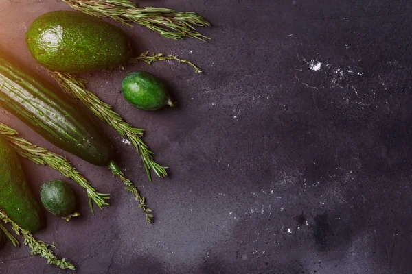 Rosemary, kimyon, salatalık, avokado, feijoa siyah arka plan üzerine. Sağlıklı gıda kavramı. Lezzetli sebze ve meyve mutfak masasında