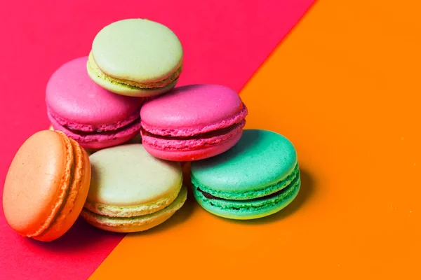 Bright pink and orange colored background for text with colorful macaroons on the edge of the photo, copy space. Application for pastry chef, confectioner
