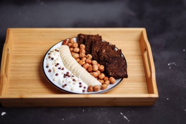 Portre sağlıklı kahvaltı tabağı çikolata parçaları, muz, çavdar ekmeği ve mutfak masasının üzerinde fındık ile yoğurt ile