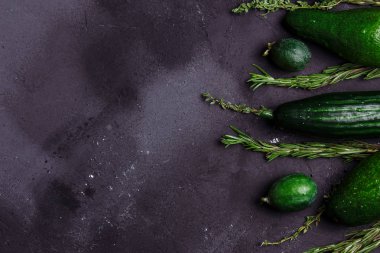 Rosemary, kimyon, salatalık, avokado, feijoa mutfak masasının üstünde siyah arka plan üzerinde. Sağlıklı gıda kavramı