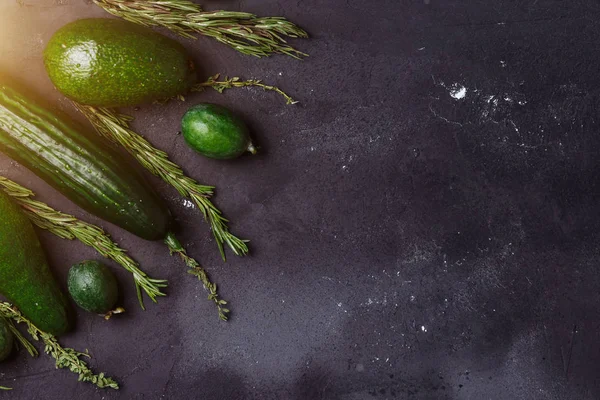 Yeşil sebze, meyve ve otlar ürün yelpazesine siyah arka plan üzerine. Alanı yukarıdan kopyalayın. Rosemary, kimyon, salatalık, avokado, feijoa mutfak masasında
