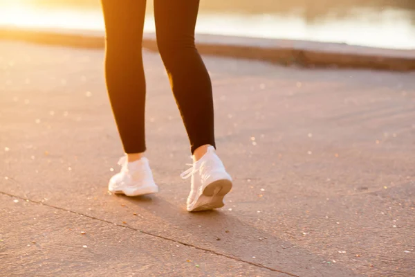 Una mujer con una figura delgada y musculosa corre con ropa deportiva negra y zapatillas blancas en la naturaleza. Recortado fotos — Foto de Stock