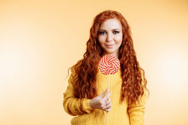 Kırmızı beyaz lolipop tutan ve gülümseyen güzel kıvırcık saçlı kadın.
