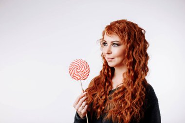 Büyük tatlı lolipop tutan ve uzak arıyorum genç ve güzel kıvırcık saçlı kadın