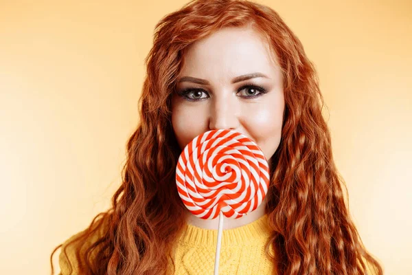 Hermosa joven mujer oculta su boca detrás de la piruleta roja blanca — Foto de Stock
