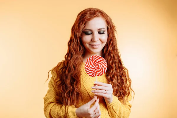 Kırmızı beyaz lolipop tutan ve aşağı bakıyor güzel genç kıvırcık Kızıl saçlı kadın.