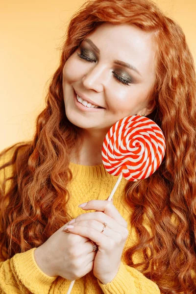 愉快的卷曲红头发的女人拿着一个红色的白色棒棒糖 — 图库照片
