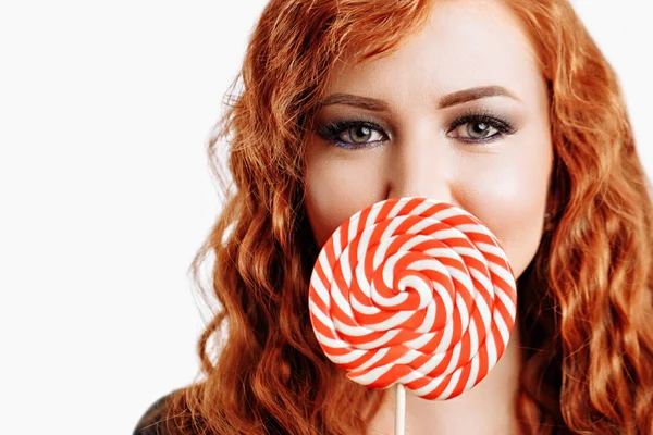 美丽的红发妇女拿着一个红色白色棒棒糖在白色背景 — 图库照片