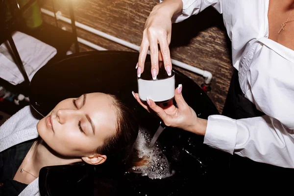 Cerca de la cara de una hermosa joven sonriente que recibe procedimientos de cuidado del cabello en el salón de belleza, sus ojos se cierran con relajación. Cuidado del cabello, productos de belleza, spa — Foto de Stock