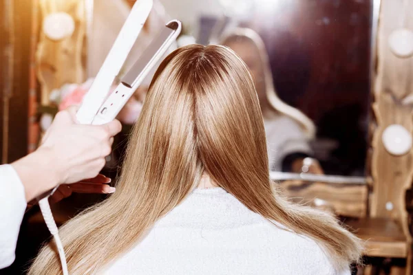 Szoros fel a folyamat hajkiegyenesítő hosszú szőke haja hajvasalót. Szépség, frizura, meleg stílus, keratin egyengető koncepció. A fodrász a női frizurát teszi — Stock Fotó