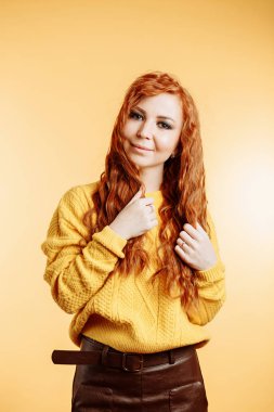 Üzerinde sarı kazaklı, kıvırcık saçları çok dokunaklı ve sevimli gülümseme ile kameraya bakarak kahverengi deri etek giymiş genç Kızıl saçlı kadın stüdyo çekim izole