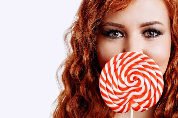 Hermosa pelirroja sosteniendo una piruleta roja blanca sobre fondo blanco — Foto de Stock