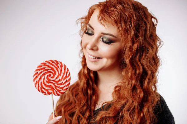 拿着大甜棒棒糖的年轻卷发红头发的女人 — 图库照片