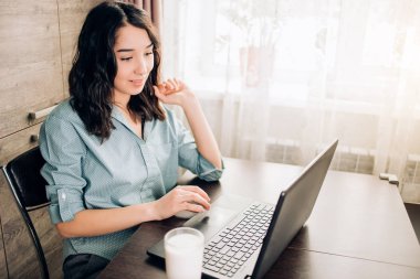 Evde dizüstü bilgisayar kullanan mutlu genç bir kadın.