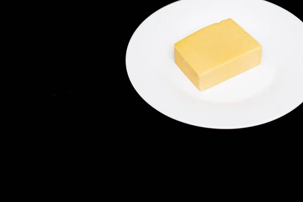 Closeup of a piece of cheese on a white plate on a black background with copy space. Natural dairy products, delicious food — Stock Photo, Image