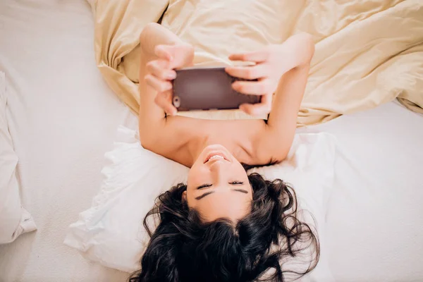 Beautiful young smiling brunette woman using phone in her bedroom