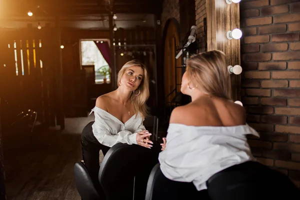 Beautiful blonde woman looking at her reflection in the mirror in beauty salon and checking new haircut and makeup. Beauty salon, showroom — 图库照片