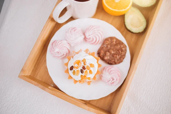 Good morning Breakfast in bed with tea, orange, avocado, cake, marshmallows, chocolate biscuits in wooden tray. lifestyle, food, meal, home comfort and relaxation